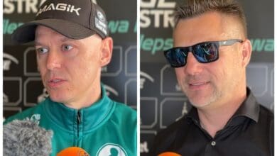 Two men in black shirts and sunglasses are talking to each other.